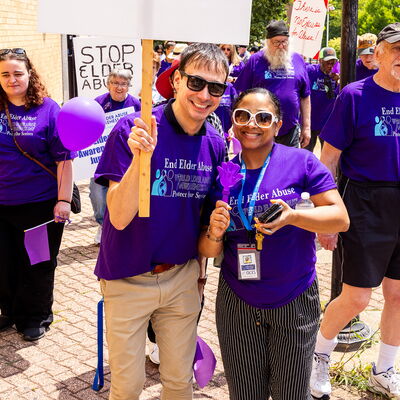 Participants march down a street in Brockton wearing purple and holding signs to raise awareness about elder abuse.